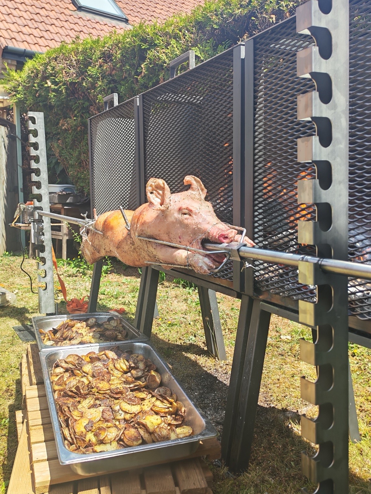 Cochon rôti à la broche au feu de bois, pommes de terre en cuisson